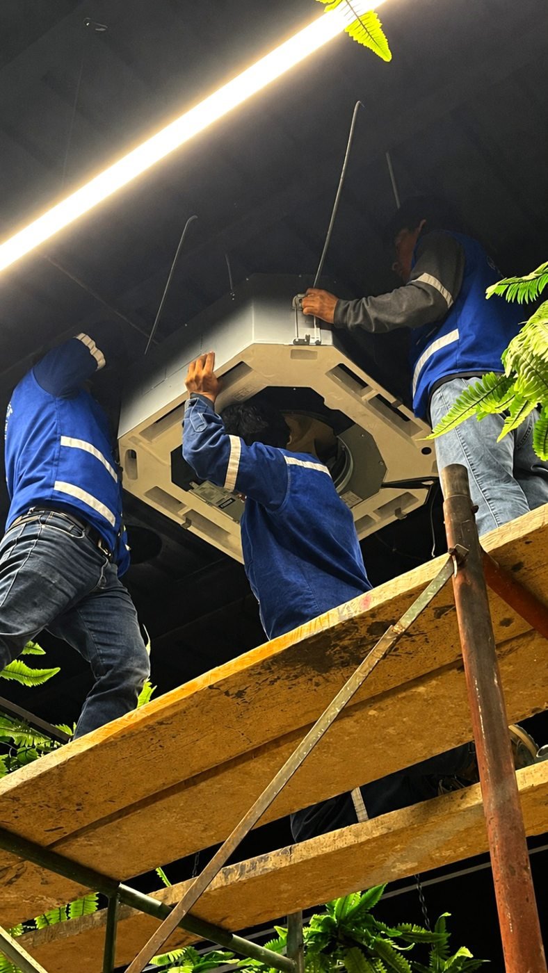 Equipo técnico de CLIMAFEL instalando un aire acondicionado tipo cassette en un local comercial.